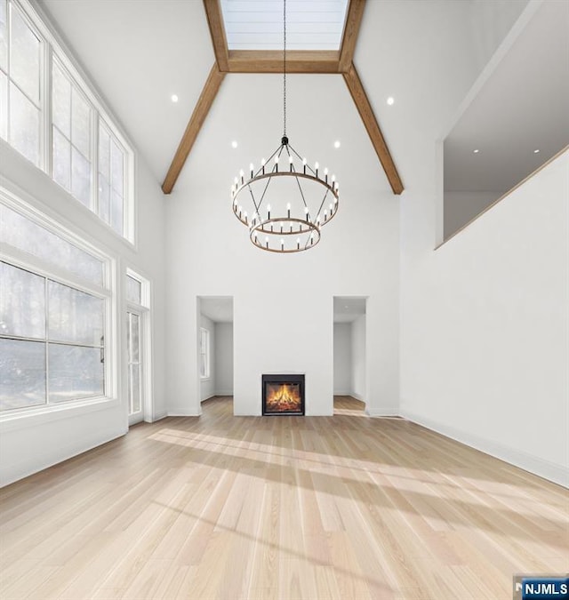 unfurnished living room featuring a glass covered fireplace, beamed ceiling, an inviting chandelier, light wood-style floors, and high vaulted ceiling