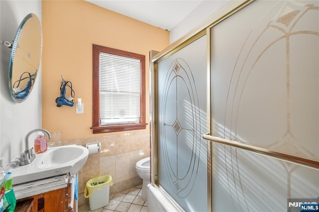 full bathroom with tile patterned floors, toilet, bath / shower combo with glass door, tile walls, and vanity