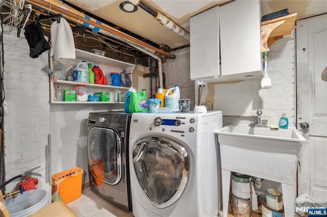 clothes washing area with independent washer and dryer, cabinets, brick wall, and sink