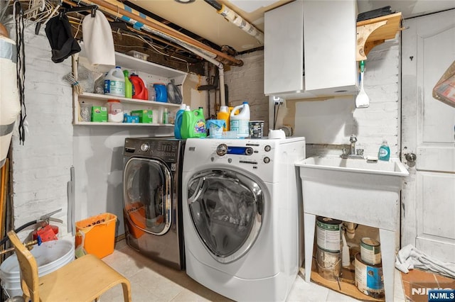 laundry room featuring cabinets, brick wall, and separate washer and dryer