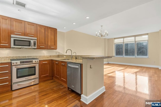 kitchen featuring sink, light wood-type flooring, appliances with stainless steel finishes, kitchen peninsula, and light stone countertops