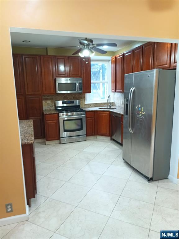 kitchen with sink, backsplash, dark stone counters, ceiling fan, and stainless steel appliances