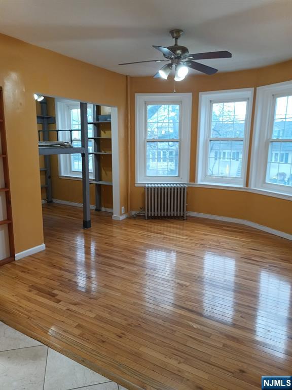 empty room with ceiling fan, radiator, and light wood-type flooring