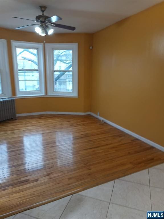 unfurnished room with ceiling fan, radiator, and light wood-type flooring