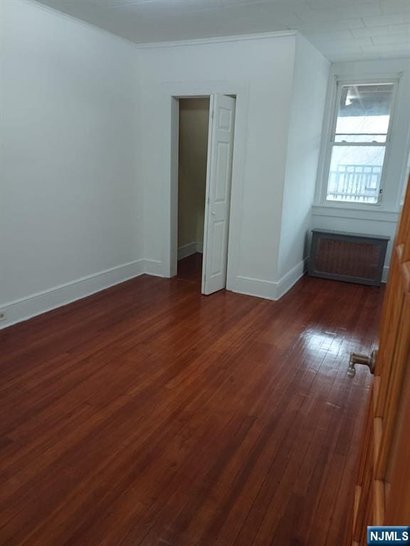 unfurnished bedroom with dark wood-type flooring and radiator heating unit