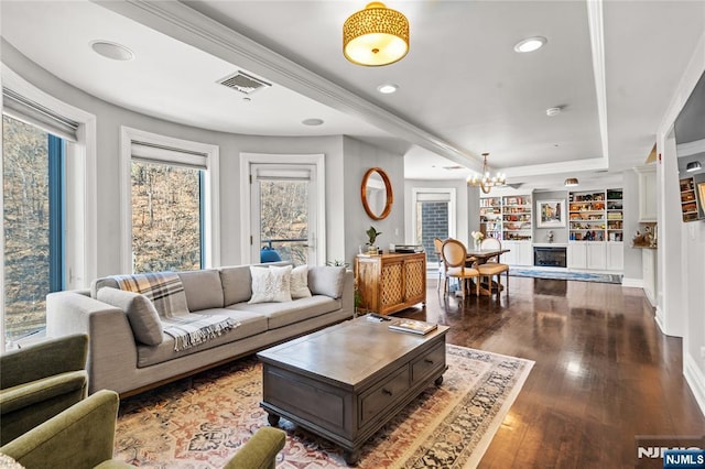 living room with built in shelves, an inviting chandelier, wood-type flooring, a tray ceiling, and a fireplace