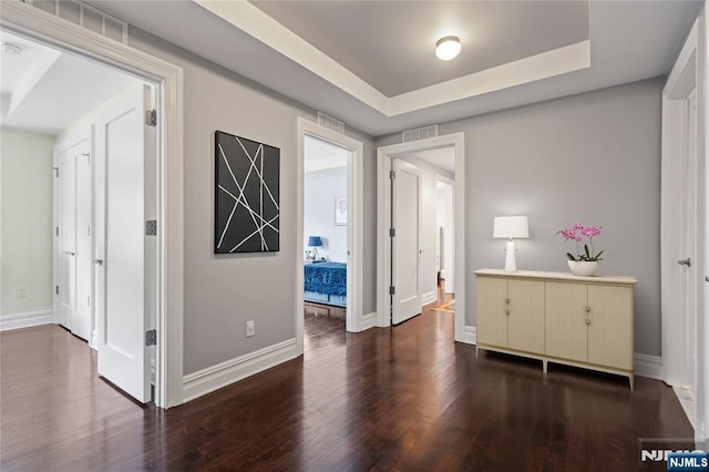 corridor with dark hardwood / wood-style flooring and a tray ceiling