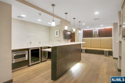 kitchen featuring dark brown cabinets, light hardwood / wood-style flooring, a kitchen island, pendant lighting, and beverage cooler