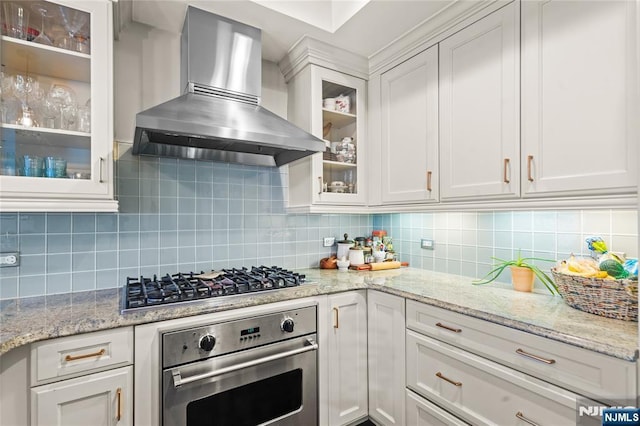 kitchen featuring white cabinets, backsplash, wall chimney exhaust hood, and appliances with stainless steel finishes