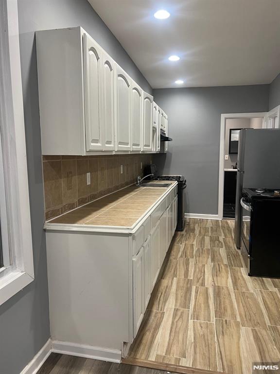 kitchen with black electric range oven, sink, white cabinetry, light hardwood / wood-style floors, and backsplash