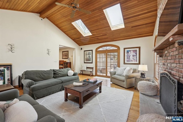 living room featuring wood ceiling, a skylight, light wood-type flooring, beamed ceiling, and a fireplace