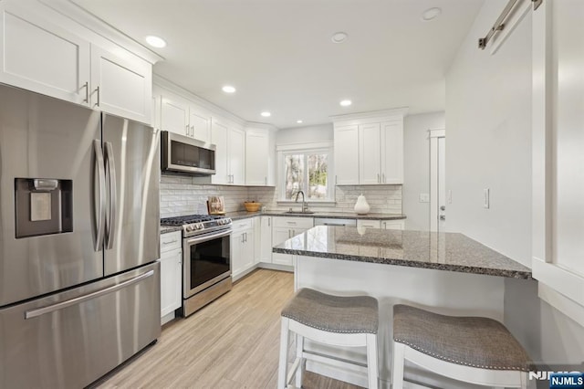 kitchen with sink, appliances with stainless steel finishes, white cabinetry, dark stone countertops, and a kitchen bar