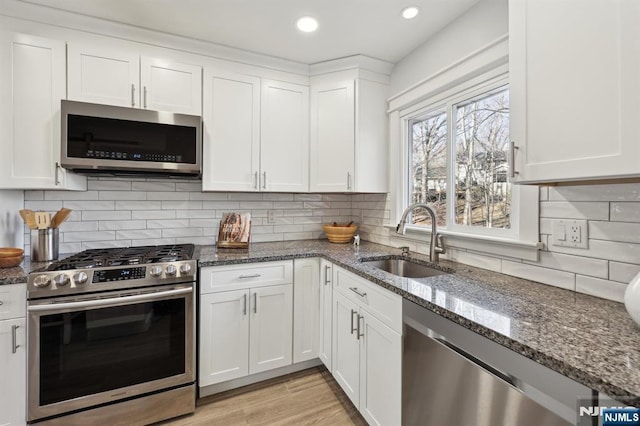 kitchen with white cabinetry, appliances with stainless steel finishes, sink, and dark stone counters