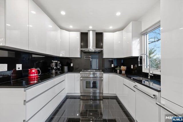 kitchen featuring sink, white cabinetry, stainless steel range, decorative backsplash, and wall chimney exhaust hood