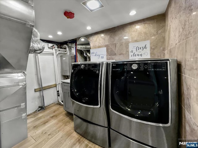 clothes washing area featuring light hardwood / wood-style floors, washing machine and dryer, water heater, and tile walls