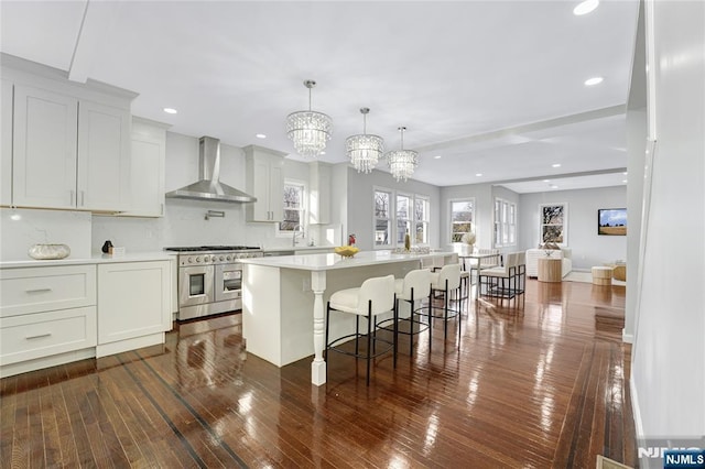 kitchen featuring white cabinetry, wall chimney exhaust hood, a center island, and range with two ovens