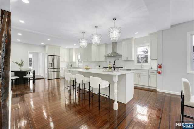 kitchen featuring white cabinetry, pendant lighting, wall chimney range hood, and stainless steel fridge with ice dispenser