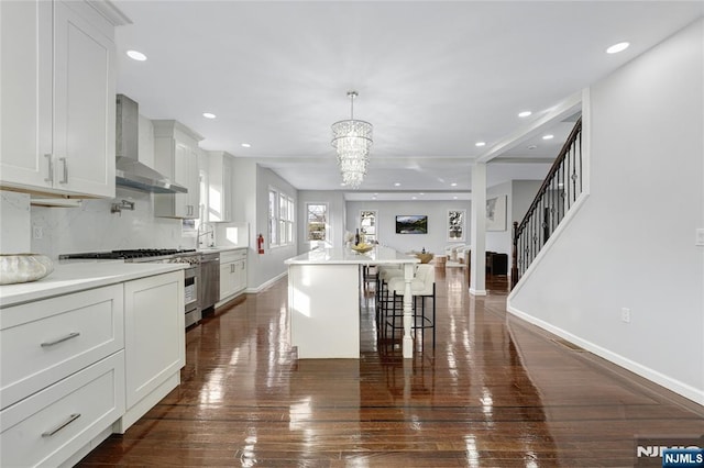 kitchen featuring pendant lighting, wall chimney range hood, a breakfast bar area, white cabinetry, and a kitchen island