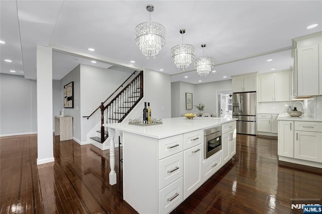 kitchen with dark wood-type flooring, hanging light fixtures, stainless steel appliances, a center island, and white cabinets