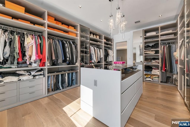 spacious closet with a notable chandelier and light hardwood / wood-style floors