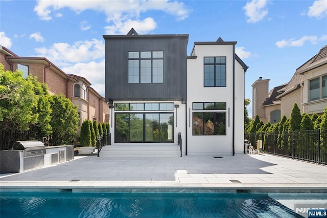 back of property featuring a fenced in pool, a patio area, and an outdoor kitchen