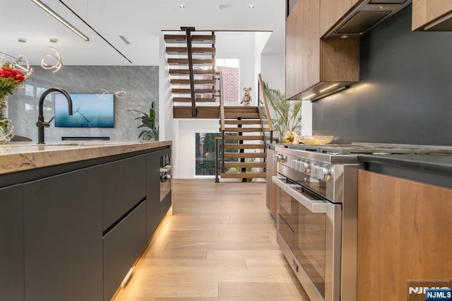kitchen with sink, backsplash, high end stainless steel range, and light hardwood / wood-style floors