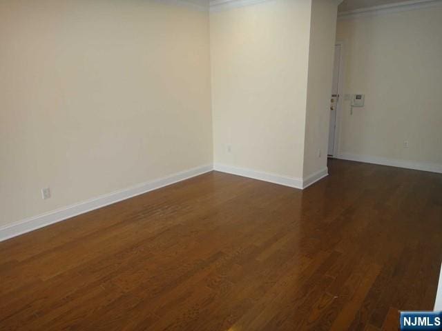 spare room with ornamental molding and dark wood-type flooring