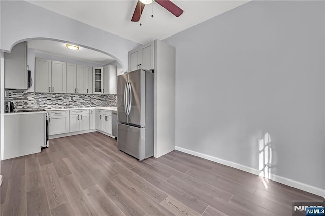 kitchen with appliances with stainless steel finishes, white cabinetry, backsplash, ceiling fan, and light hardwood / wood-style floors