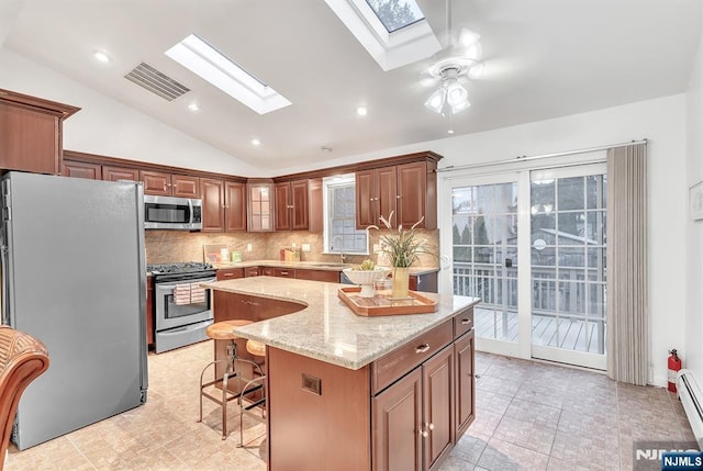 kitchen featuring a kitchen bar, lofted ceiling with skylight, a center island, appliances with stainless steel finishes, and light stone countertops