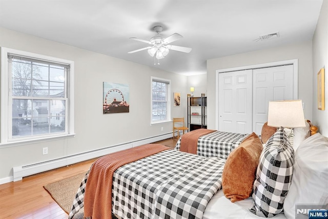 bedroom featuring a baseboard heating unit, wood-type flooring, a closet, and ceiling fan