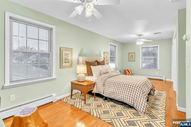 bedroom with multiple windows, hardwood / wood-style flooring, and baseboard heating