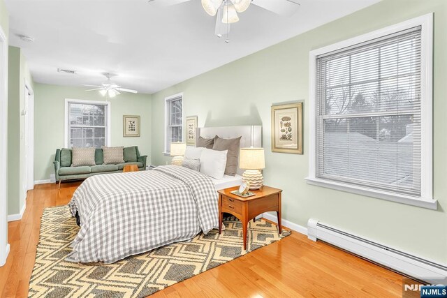 bedroom featuring a baseboard heating unit, hardwood / wood-style floors, and ceiling fan