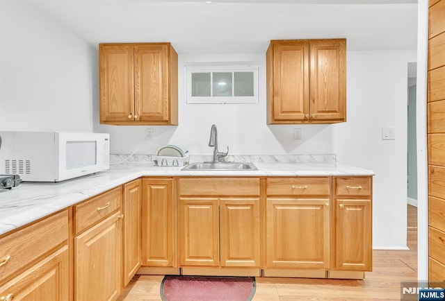 kitchen with sink, light stone counters, and light wood-type flooring