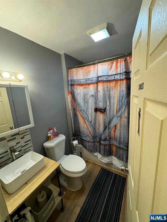 bathroom featuring decorative backsplash, wood-type flooring, toilet, and a shower with shower curtain