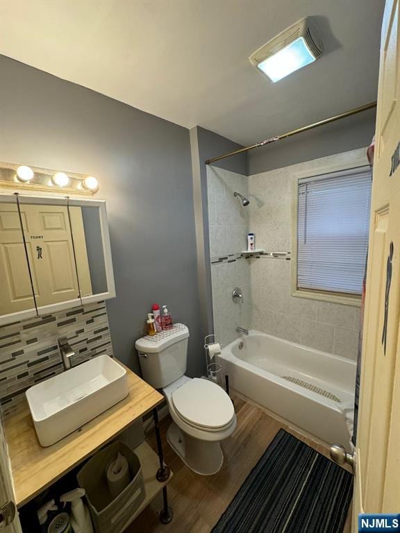 full bathroom with backsplash, tiled shower / bath combo, vanity, wood-type flooring, and toilet