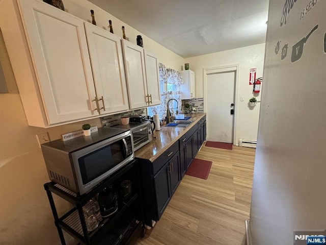 kitchen with a baseboard heating unit, light hardwood / wood-style floors, sink, and white cabinets