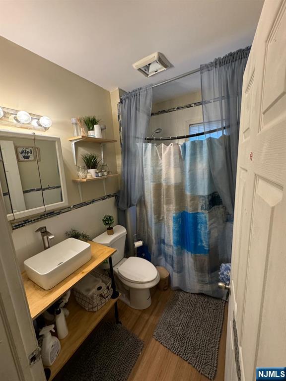 bathroom with vaulted ceiling, wood-type flooring, sink, toilet, and a shower with shower curtain