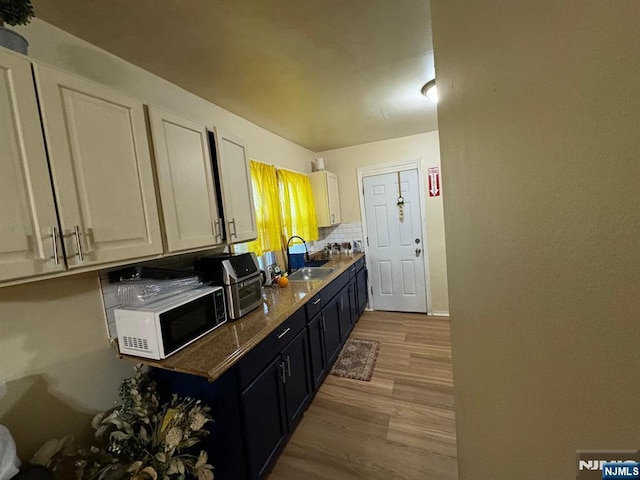 kitchen featuring backsplash, light hardwood / wood-style floors, sink, and white cabinets