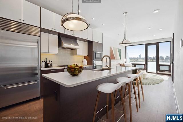 kitchen featuring ventilation hood, an island with sink, pendant lighting, and built in appliances