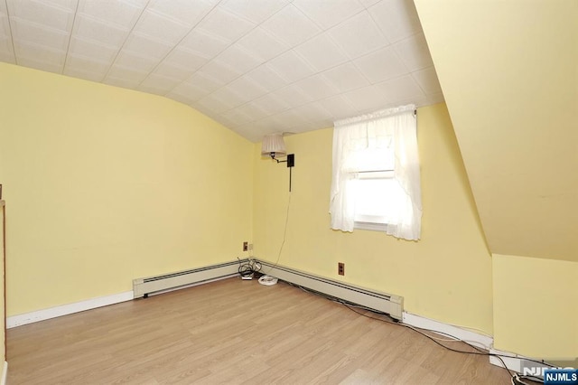 spare room featuring a baseboard radiator, vaulted ceiling, and light wood-type flooring