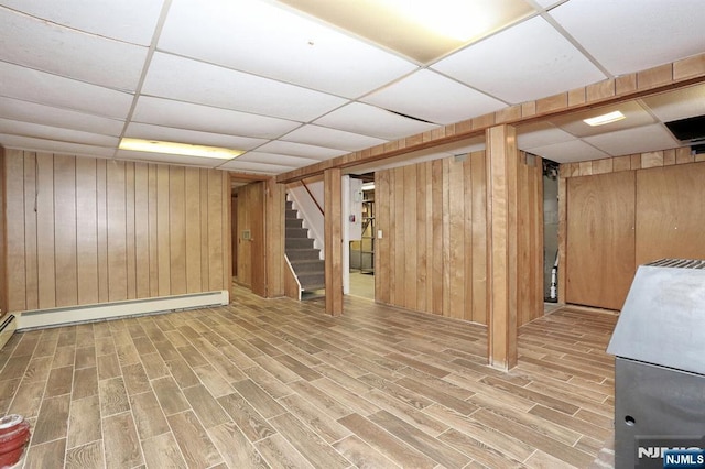 basement with a baseboard heating unit, a paneled ceiling, and wooden walls