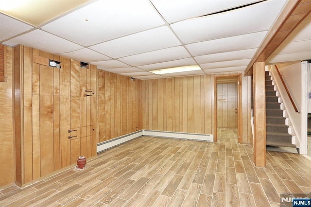 basement featuring hardwood / wood-style flooring, a baseboard radiator, a paneled ceiling, and wood walls