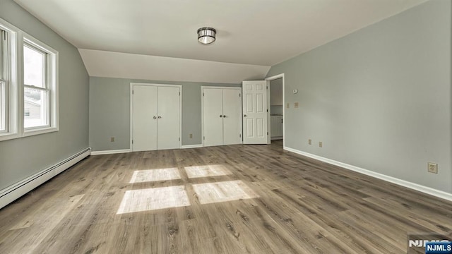 unfurnished bedroom featuring two closets, vaulted ceiling, and light hardwood / wood-style floors