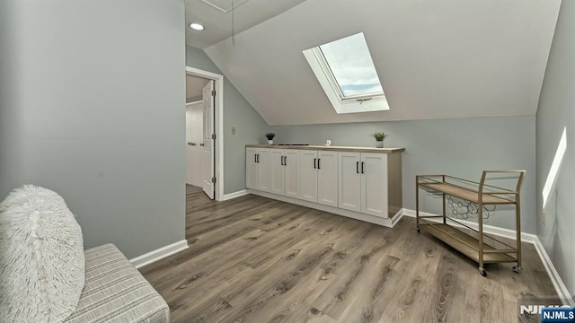 interior space featuring lofted ceiling with skylight and light hardwood / wood-style flooring