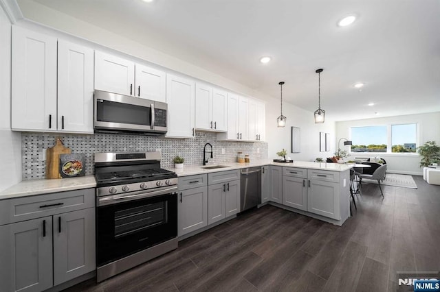 kitchen with sink, gray cabinetry, appliances with stainless steel finishes, kitchen peninsula, and pendant lighting