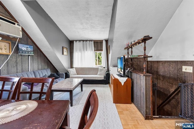 living room with light parquet flooring, wooden walls, a wall unit AC, and a textured ceiling