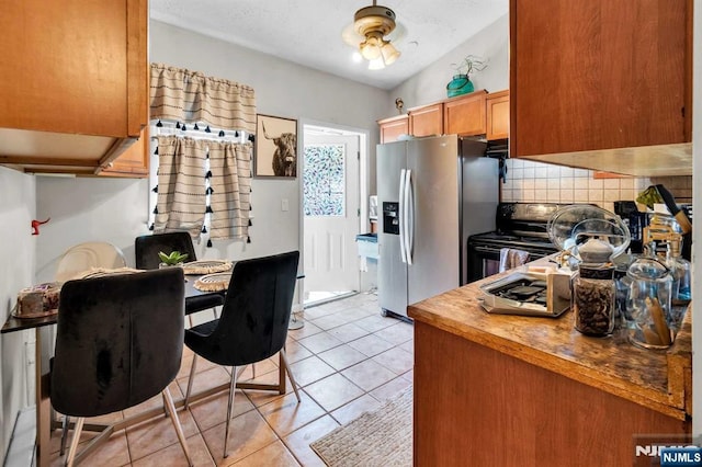 kitchen featuring vaulted ceiling, tasteful backsplash, stainless steel fridge, light tile patterned floors, and black electric range