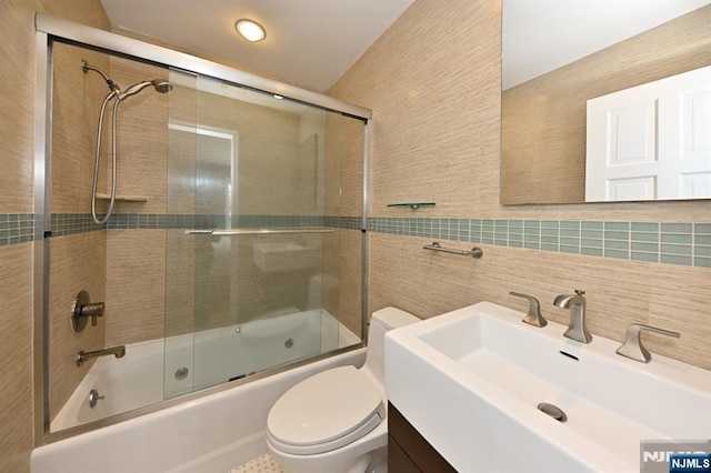 full bathroom featuring shower / bath combination with glass door, tile walls, vanity, decorative backsplash, and toilet