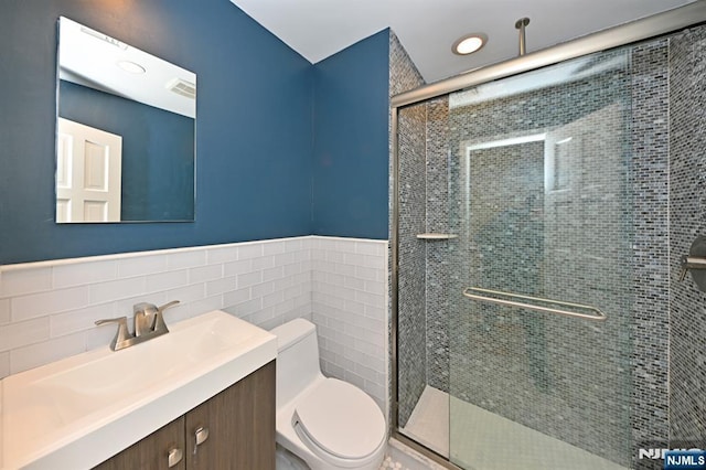 bathroom with vanity, a shower with door, tile walls, and toilet