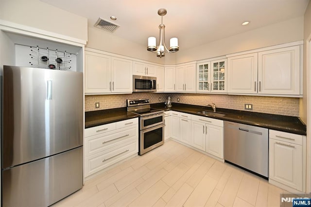 kitchen featuring sink, white cabinetry, a chandelier, stainless steel appliances, and decorative backsplash